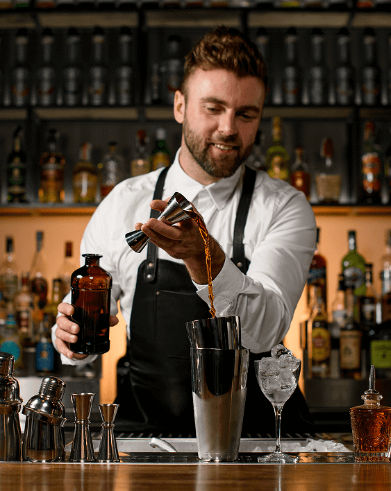 Bartender pouring drink into cocktail shaker.