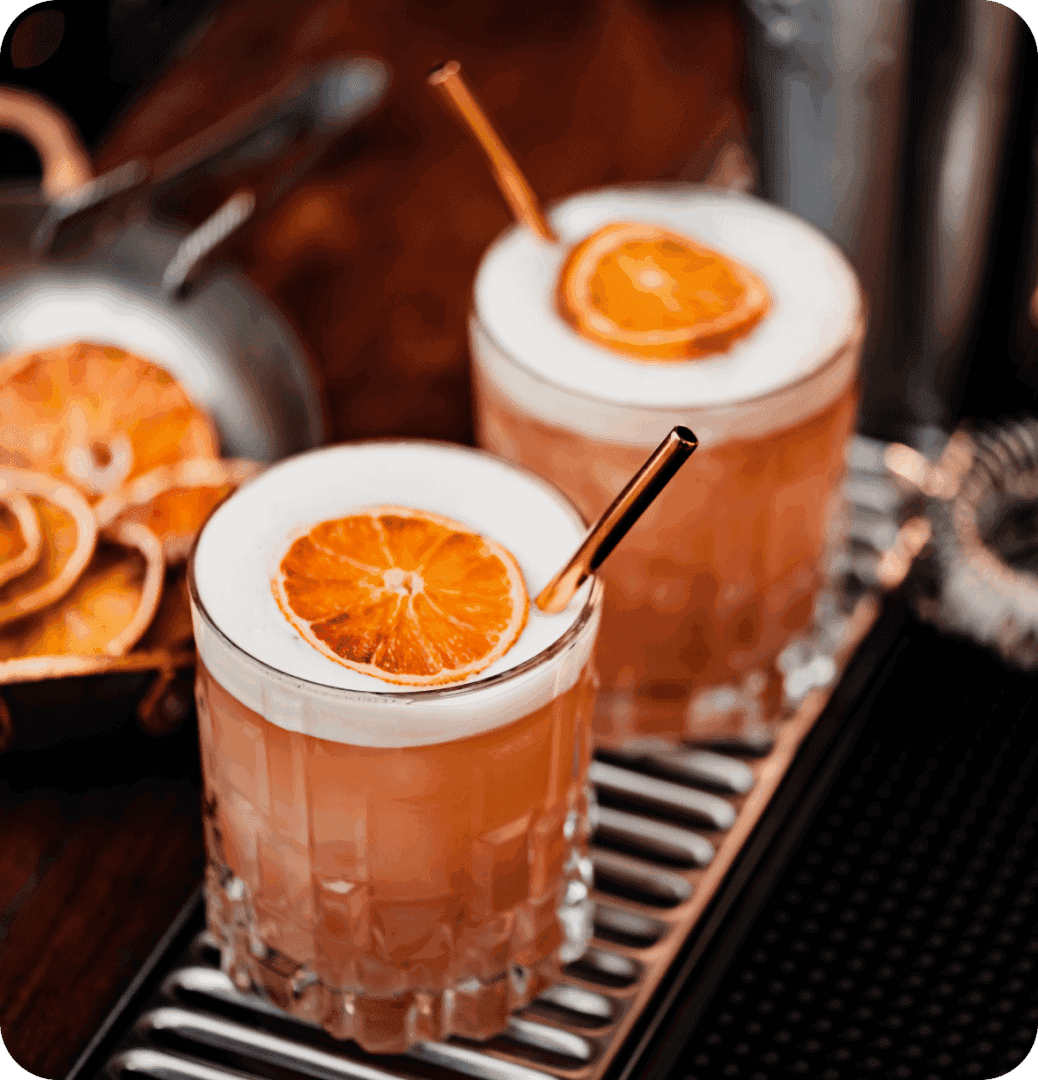 Two cocktails with orange garnishes on bar.